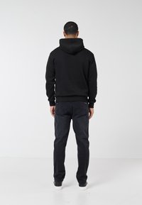 Svart hoodie med en kanguruficka och huva med dragsko. Kombinerad med mörka jeans och svarta skor, visad bakifrån.