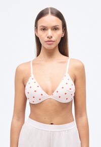 Τριγωνικό σουτιέν χωρίς ραφές από απαλό ύφασμα, σε ανοιχτό ροζ με μικρά κόκκινα σχέδια καρδιάς, με λεπτές ρυθμιζόμενες τιράντες και κυματιστά τελειώματα.