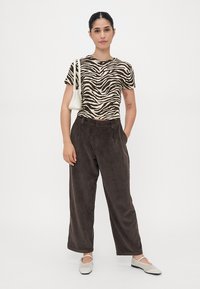 T-skjorte med zebra-print i beige og brunt, paret med brune kordfløyelsbukser med vide ben. Hvit håndveske og lys fottøy fullfører antrekket.