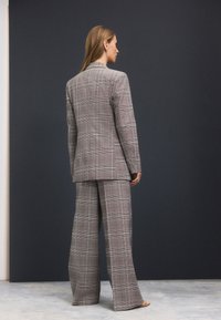 Grey checked suit made of fabric; features a long blazer with notched lapels and wide-leg trousers, textured pattern, minimalist design.