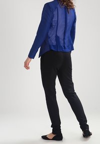 Blå strukturerad blazer med meshinspirerad rygg, kombinerad med svarta figurnära byxor och svarta ballerinas. Enkelt design med kontrasterande material.