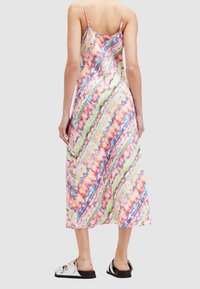 Robe maxi en satin avec un motif tie-dye multicolore, des bretelles spaghetti et une silhouette fluide. Associée à des sandales plates noires.