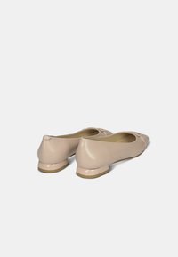 Beige bőr balerina cipők enyhe sarokkal, lekerekített orral, elöl dekoratív masnival. Simább textúra fényes kiegészítéssel.