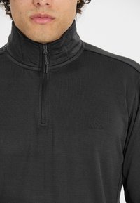 Schwarzer Viertelzip-Pullover aus strukturiertem Stoff. Verfügt über einen hohen Kragen und ein kleines Logo auf der Brust. Reißverschluss mit einem Stoff-Zugband.