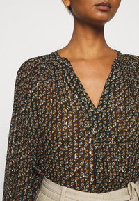 Černá blůza s vzorem a malými květinovými motivy v oranžové a tyrkysové barvě, s výstřihem do V a sklady na ramenech.