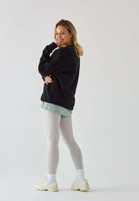 Czarny sweatshirt, jasnozielony top warstwowy, jasnoszare legginsy i beżowe sneakersy. Gładka tekstura, luźny krój i długość do kostek.