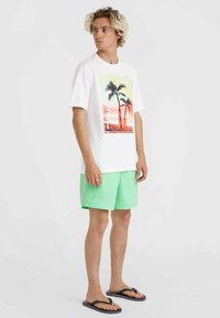 Camiseta blanca de manga corta con gráfico de palmera en naranja y amarillo, combinada con pantalones cortos verde menta y chanclas negras.