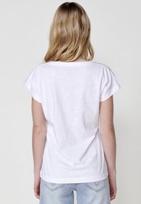Camiseta blanca de manga corta con un corte relajado, presenta un escote redondeado y un tejido suave y ligero. Textura lisa, detalle de costura mínima.
