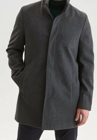 Grauer Fischgrätmantel mit Stehkragen, vorderer Knopfleiste, zwei Seitentaschen und glatter Textur. Lange Ärmel mit enganliegenden Bündchen.