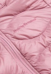 Giacca puffer rosa chiaro con dettagli di cucitura, una superficie liscia e chiusura con zip. Il nome del marchio "PeakPerformance" è ricamato in rosa.