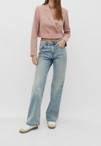 Cropped pink blazer with double buttons, paired with light blue wide-leg jeans and white sneakers. Smooth fabric, relaxed fit.