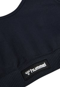 Nahaufnahme von navy-blauem, geripptem Funktionsstoff mit schwarzem rechteckigem Hummel-Logo-Patch mit weißem Bienen-Symbol und Schriftzug.