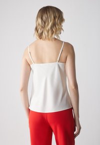 Camiseta de satén blanca con tirantes finos ajustables, textura suave y un corte ligeramente holgado, combinada con pantalones rojos vibrantes.