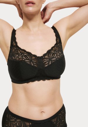 Reggiseno in pizzo nero con design a pois, bordi scallop e un fiocco decorativo al centro. Spalline spesse per un maggiore supporto e comfort.