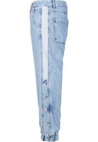 Joggings din denim de culoare albastră deschisă, cu o dungi albe contrastante pe lateral, mai multe butoane la gleznă și un buzunar aplicat pe spate.