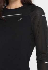 Camiseta atlética negra de manga larga con textura de malla en las mangas, con acentos grises reflectantes y un logo en el pecho.