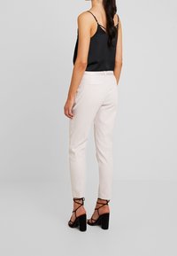 Pantalons ajustés roses clairs en tissu lisse. Associés à un top cami en satin noir et des talons noirs à lanières.