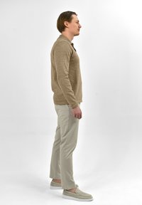 Beige polo shirt met lange mouwen, gemaakt van gestructureerde stof, gecombineerd met lichtgekleurde, nauwsluitende broeken en lichtgrijze instappers.