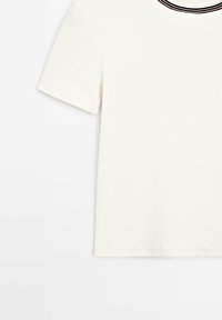 Haut court à manches courtes rayé blanc avec un col rond agrémenté d'une bordure noire et colorée. Tissu doux avec une texture lisse.