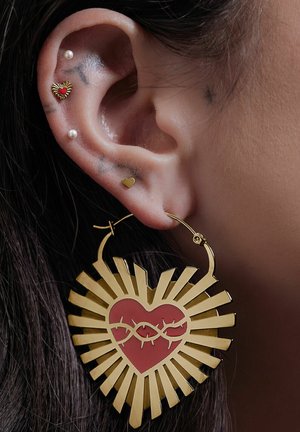 Goldene Creolen mit einem großen Herzensdesign, das ein rotes Zentrum hat, umgeben von strahlenden Streifen. Kleine Herz- und Perlen-Stecker sind ebenfalls sichtbar.