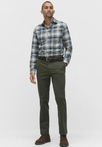Mans långärmad rutigt skjorta i blått och vitt, kombinerad med olivgröna byxor. Har en knapp-down krage och ett brunt bälte. Bruna stövlar fulländar outfiten.
