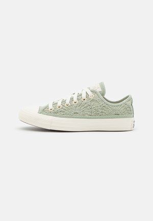 Baskets basses vert clair avec superposition de dentelle florale, semelle et embout en caoutchouc blanc, et lacets blancs avec œillets dorés.