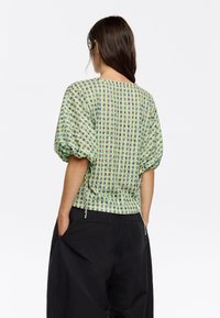 Groene en gele gebloemde blouse met pofmouwen, gestructureerde stof en aansnoerdetail in de taille. Achteraanzicht weergegeven.