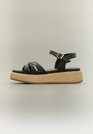 Mustast nahast platvormsandal kootud beežide tallaga, avatud varbaga, kolm esimest rihma ja reguleeritav pahkluu rihm kuldse pandlaga.