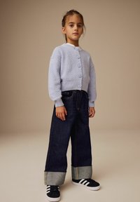 Hellblauer strukturierter Strickcardigan mit fünf Knöpfen, kombiniert mit übergroßen dunklen Jeans aus Denim mit umgeschlagenen Säumen und schwarzen Sneakern.