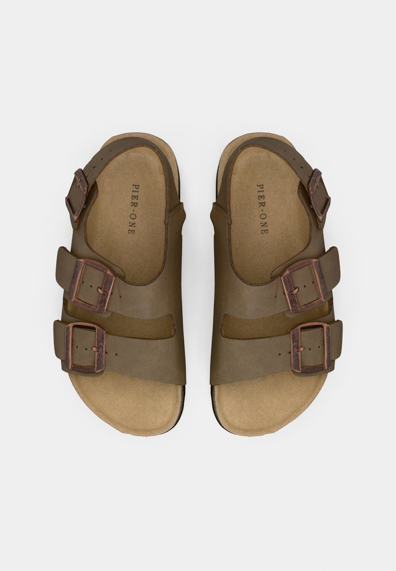 Sandales en cuir marron avec trois sangles réglables, boucles en bronze et semelle rembourrée. Semelle plate conçue pour le confort et la stabilité.