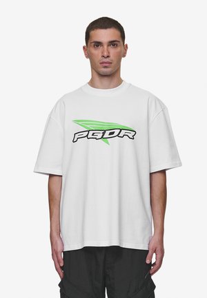 White oversized t-shirt with short sleeves featuring a black and green graphic text "PGDR" on the front. Smooth cotton texture.