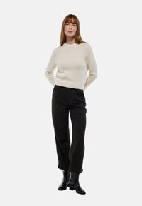 Pull en tricot crème avec une finition texturée, associé à un pantalon à carreaux sombre et des bottines noires. Le pull a un col rond et un ourlet côtelé.