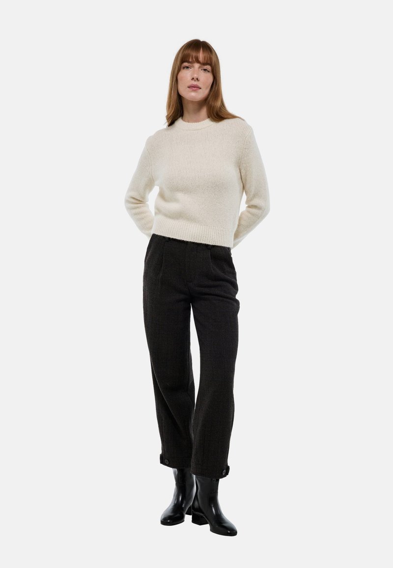 Pull en tricot crème avec une finition texturée, associé à un pantalon à carreaux sombre et des bottines noires. Le pull a un col rond et un ourlet côtelé.