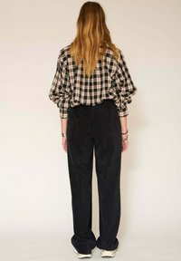 Chemise oversize à carreaux en noir, beige et blanc avec des manches amples, associée à un pantalon en velours côtelé foncé taille haute, mettant en valeur un tissu texturé.