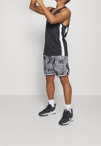 Débardeur de sport noir avec des rayures blanches sur les côtés, associé à un short à motifs noir et blanc avec un design texturé. Chaussures de sport noires.