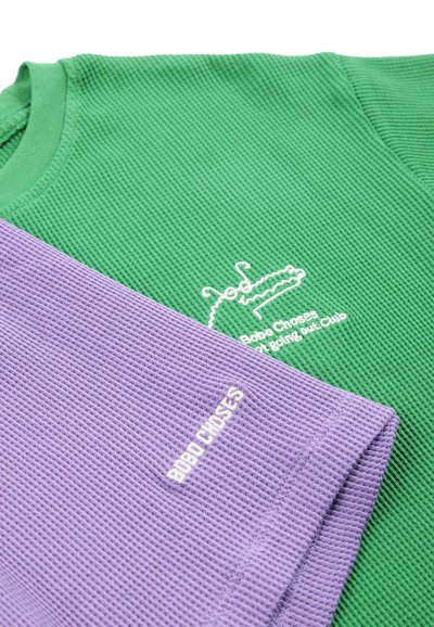 Magliette lavorate a maglia verde e viola con scritta bianca "Bobo Choses" e un piccolo ricamo sul petto della maglietta verde.