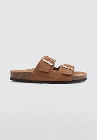 Sandales en suède marron avec deux sangles réglables à boucle, un lit de pied en liège contourné et une semelle extérieure en caoutchouc noir texturé.