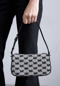 Black and gray canvas handbag featuring repeated "MK" logo pattern, slim design, and a short black shoulder strap. Zipper closure at top.
