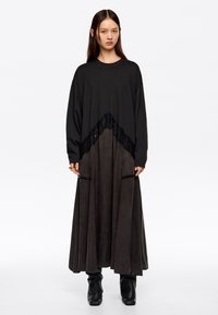 Długa czarna sukienka z fakturowanym detalem koronkowym w pasie. Spódnica ma luźną sylwetkę, wykonaną z miękkiego materiału o matowym wykończeniu.