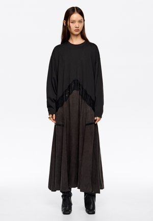 Vestido negro largo con un detalle de encaje texturizado en la cintura. La falda tiene una silueta fluida, hecha de un tejido suave con acabado mate.