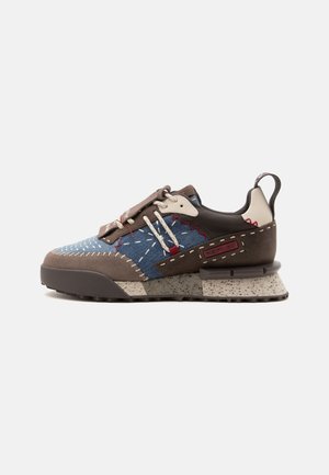 Low-top sneaker met blauwe denim, bruin suède, rode stiksels, crème veter, gevlekte zool en een bruine trek-lus op de hiel.