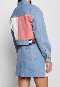 Kvinna iklädd en ljusblå denimjacka med röd och vit panel och matchande denimkjol med fickor och fransad fåll.