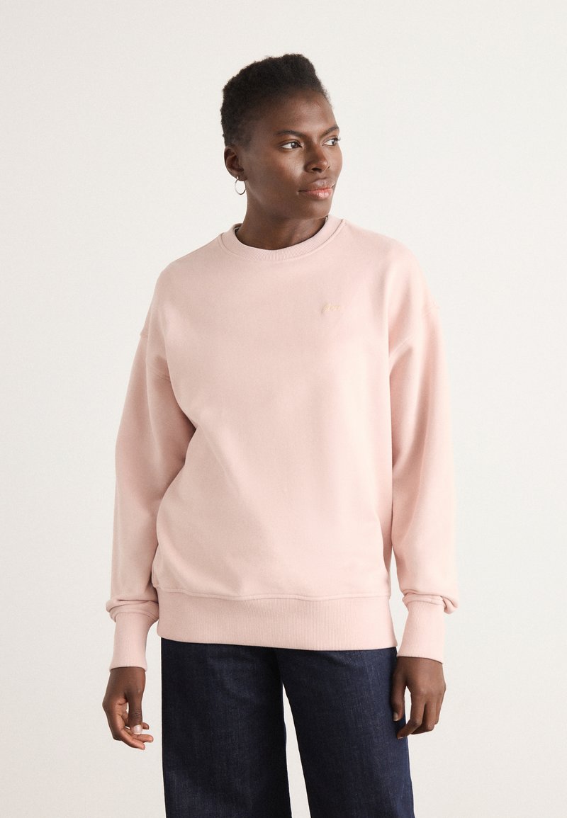 Lys rosa sweatshirt med rund hals, ribbestrikkede mansjetter og subtil logo-detallering på brystet. Mykt stoff med en avslappet passform.