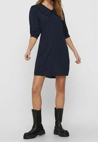 Námořnické modré šaty s bílými puntíky, s velkým límečkem a tříčtvrtečními rukávy. Nosené s černými robustními botami pro kontrast.