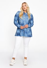 Denim-like button-up shirt in blue with a gradient pattern, long sleeves, and a curved hem, paired with white pants and light sneakers.