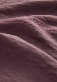 Gros plan d'un tissu mauve doux et froissé montrant la texture et les plis avec un éclairage naturel.