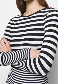 Black and white striped long-sleeve top with a round neckline. Features gold-button accents on the shoulder. Cotton blend material.
