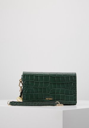 Clutch de cuero verde oscuro con textura de cocodrilo, herrajes dorados y correa de muñeca desmontable, colocado sobre una plataforma blanca.