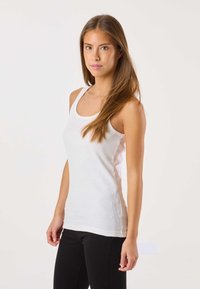 Valkoinen ribbineuloksinen toppi, jossa on pyöreä pääntie, istuva siluetti ja sileä pinta; yhdistetty mustiin kapeisiin farkkuihin.