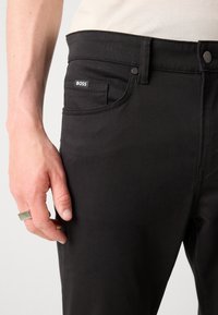 Zwarte denim broek met een knoopsluiting, slim fit, met een klein "BOSS" label op de voorzak en een gladde textuur.